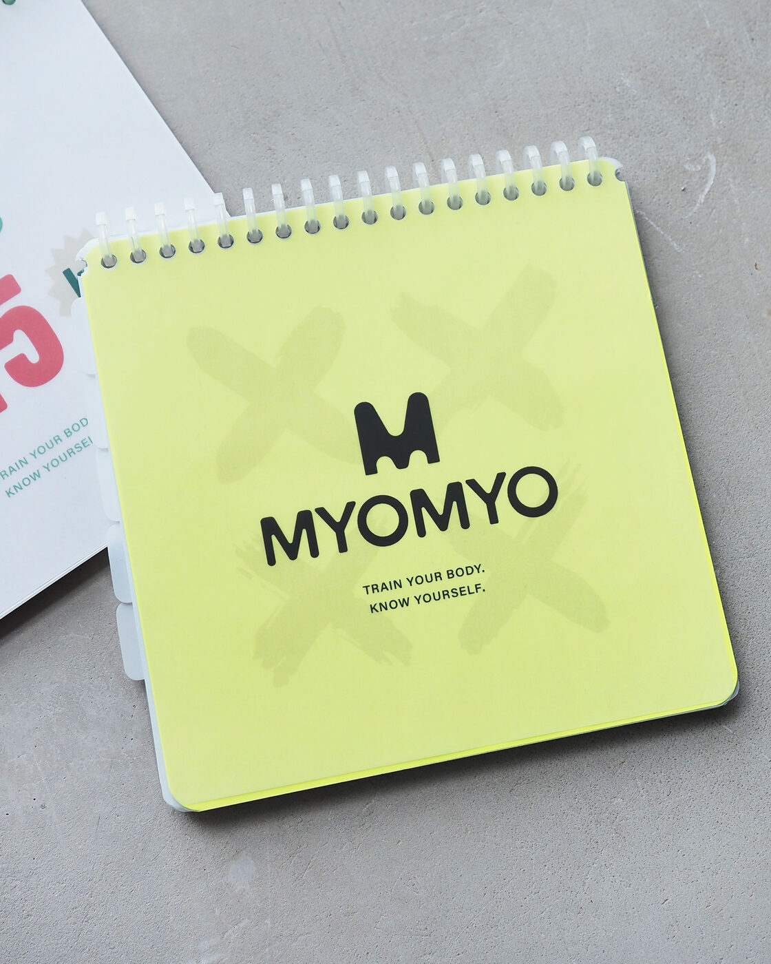 コンクリートの上に置いたネオンイエローのMYOMYOトレーニング手帳
